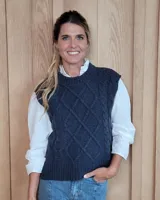 Chaleco de punto color gris oscuro, con diseño de trenzas y rombos en el frente. Presenta cuello redondo, sisas amplias y terminaciones en tejido acanalado.