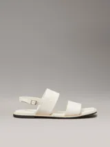 Sandalias planas blancas de cuero sintético, con puntera cuadrada y dos tiras anchas. La tira superior tiene el logo de Calvin Klein grabado.
