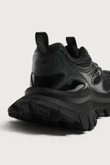 Zapatilla deportiva tipo running de color negro, confeccionada con una combinación de materiales y piezas, con suela robusta de gran volumen y diseño irregular.