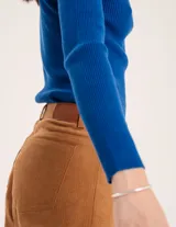 Pantalón de pana color verde oliva, de corte wide leg y largo al tobillo. Tiene cierre delantero con botón, bolsillos laterales y traseros.