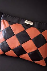 Cartera tipo sobre con diseño de ajedrez en rombos de cuero blanco y negro. Cuenta con una correa de mano integrada y detalle de placa metálica con logo.