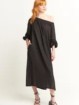 Vestido largo color beige, con escote elastizado que permite usarlo con los hombros descubiertos, mangas largas abullonadas, bolsillos laterales y tajos laterales en el ruedo.