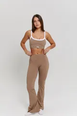 Conjunto deportivo compuesto por un top y un pantalón largo color habano. El top es de escote redondo con breteles blancos y detalle de logo 'bk.' en el frente. El pantalón es de tiro alto con costuras laterales blancas y corte ligeramente acampanado en el ruedo.