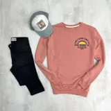 Buzo color salmón de algodón con cuello redondo, puños y cintura acanalados. Estampado en el frente con un sol y el texto "Only Good Vibes Surf Duxon Co. 3-77 Vissla St. California, USA 92672".