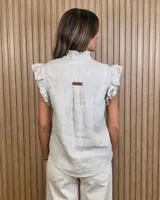 Musculosa de jean celeste sin mangas, con cuello alto fruncido, cierre frontal con botones y detalles de volados en las sisas y a lo largo de la botonera.