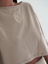 Top corto azul marino de punto, con mangas cortas amplias, cuello redondo y detalle de escudo bordado en la parte delantera.