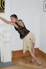 Falda corta de tiro bajo confeccionada en tul color beige, con capas, bajo asimétrico, bordados florales oscuros con lentejuelas en contraste y cierre lateral con nudo.