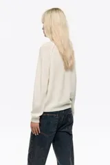 Sweater de punto color blanco, de corte oversize y escote redondo. Presenta mangas largas y detalles calados en las sisas. Confeccionado en una mezcla de acrílico y lana.