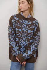 Buzo de tejido de punto en color marrón con un patrón ornamental floral en color celeste. Presenta cuello redondo, mangas largas y un corte holgado.