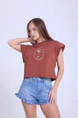 Remera color ladrillo de algodón, de corte crop y mangas cortas con efecto hombrera. Estampado frontal con palmera y texto en blanco.