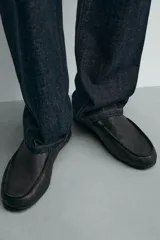 Mocasín de cuero negro, de estilo clásico y minimalista, con suela fina y horma cuadrada.