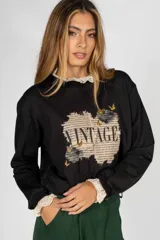 Sweater negro de algodón con cuello y puños de encaje, y estampado frontal con la palabra "Vintage" sobre un fondo de texto antiguo.