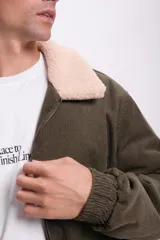 Campera bomber verde de pana con cuello de piel sintética color crema, cierre frontal con cremallera, bolsillos laterales con solapa y puños y cintura elastizados.