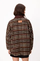Chaqueta de corte holgado con estampado de cuadros en tonos marrones, blancos y negros. Presenta cuello de pana en color marrón oscuro, cierre frontal con botones metálicos y bolsillos laterales amplios.