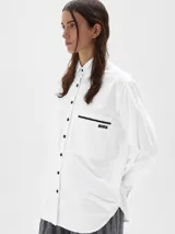 Camisa de corte oversize confeccionada en tela oxford de algodón. Presenta cuello clásico, cierre frontal con botones, mangas largas con puños y un bolsillo frontal con etiqueta de marca.