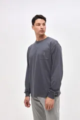 Remera de manga larga en color gris oscuro, confeccionada en algodón pesado con textura suave. Presenta un bolsillo frontal en el pecho con un pequeño bordado de la marca y puños elásticos en las mangas.