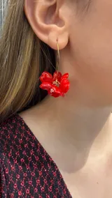 Caravana tipo argolla dorada con dije colgante en forma de flor de pétalos rojos brillantes y centro con pequeña perla.