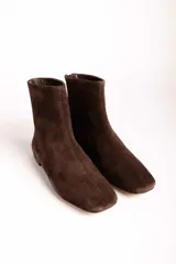Botas cortas de gamuza color marrón, con punta cuadrada y cierre lateral. Diseño minimalista con costura central vertical.