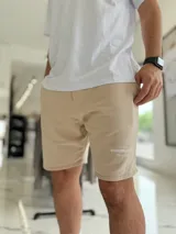 Bermuda de jogging color beige, con bolsillos laterales y estampa con texto blanco en la pierna izquierda.