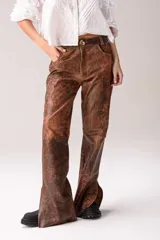 Pantalón de cuero vacuno negro, de corte recto y tiro medio. Presenta costuras horizontales a la altura de la rodilla y aberturas laterales en el ruedo. Incluye un botón de guampa irregular como detalle distintivo en la cintura.