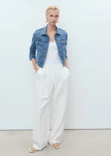 Chaqueta de jean azul de corte crop, con cuello camisero, cierre frontal de botones metálicos, bolsillos con solapa en el pecho y mangas largas con puños abotonados.