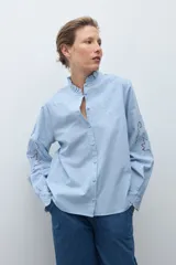 Camisa blanca de manga larga con cuello alto fruncido y bordados calados en el pecho y los hombros.
