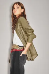 Camisa de cuero ovino color verde oliva, con cuello clásico, cierre frontal con botones y mangas largas con puños abotonados. Presenta un corte holgado y diseño tipo sobrecamisa.