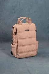 Mochila capitoneada color beige, con asa superior y correas regulables. Cuenta con doble cierre principal, un bolsillo frontal con apertura vertical, un bolsillo trasero pequeño y un compartimento interno para laptop de 15 pulgadas. Las correas son ocultables.