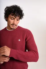 Sweater de punto grueso con cuello redondo y manga larga. Presenta un diseño de tejido acanalado y el logo de la marca bordado en el pecho.