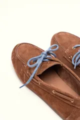 Mocasín tipo boat shoe color marrón, confeccionado en cuero, con cordones de cuero marrón y cordones decorativos azules.