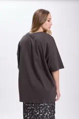 Remera de manga corta oversize color gris oscuro con estampa fotográfica de palmeras y edificio rosado.