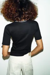Camiseta de punto ajustada con cuello redondo y manga corta. Presenta detalles de vivos en color blanco a contraste en el cuello y la tapeta frontal, que cuenta con cierre de botones metálicos.