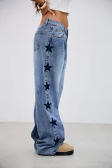 Pantalón de jean tiro medio con corte recto y holgado, presenta bordados de estrellas oscuras a lo largo de los laterales externos.