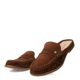 Zuecos de gamuza marrón estilo mocasín, abiertos en el talón con diseño slip-on. Presentan costuras pespunteadas visibles, detalle de tira sobre el empeine con un aplique metálico dorado y suela plana.