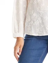 Blusa de algodón con diseño de broderie floral, cuello a la base, cierre frontal con botones y mangas largas amplias.
