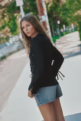 Camisa de cuello solapa con escote en pico y manga larga acabada en puño con abertura y lazo, confeccionada en tejido semitransparente de color negro con aplicación de tachas delanteras, cintura entallada con frunces laterales y cierre frontal con lazos.