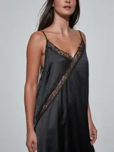 Vestido midi negro de satén con detalles de encaje en el escote, el ruedo y una aplicación diagonal que cruza el diseño. Cuenta con tirantes finos y un corte fluido.