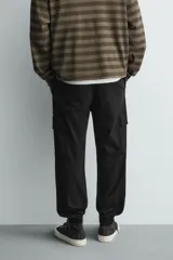 Pantalón cargo de corte slim fit en color negro, confeccionado en tejido de algodón con elasticidad. Presenta cintura elástica ajustable con cordón, bolsillos laterales tipo cargo con solapa y bajo acabado en puño elástico.