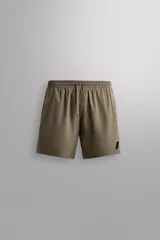 Short deportivo Zara Athleticz de color marrón, confeccionado en tejido técnico ligero y elástico con forro interior. Cuenta con cintura elástica ajustable con cordón, bolsillos frontales, bolsillo trasero con cierre de cremallera, bajo con aberturas laterales y detalle de logo estampado en la pierna.