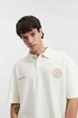 Remera polo color crema con logo bordado en el pecho, de corte amplio y mangas cortas.