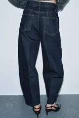 Jeans de tiro alto con corte barrel y diseño tapered, confeccionados en denim con efecto lavado y detalle de raya planchada. Presentan cintura con trabillas, cierre frontal con cremallera y botón, y bolsillos funcionales en delantero y espalda.