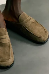 Zueco de hombre fabricado en piel con acabado serraje en color marrón claro. Presenta un diseño destalonado con detalle de antifaz en el empeine, horma redonda y suela plana a contraste.