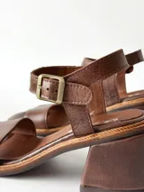 Sandalias de cuero color chocolate, con taco cuadrado de 6 cm, tira ancha en la parte delantera y tira en el tobillo con hebilla metálica ajustable.