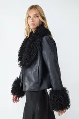 Campera corta de efecto cuero negro con cuello y puños de pelo sintético voluminoso. Presenta un diseño de corte recto y cierre frontal oculto.