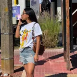 Remera blanca de corte clásico con estampa frontal ilustrada que representa un cóctel Spritz, incluyendo texto alusivo y detalles en tonos amarillos, naranjas y rojos con efecto de pinceladas.