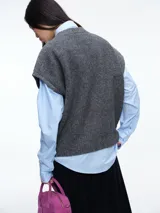 Chaleco de tejido de punto color gris, con cuello redondo y cierre frontal completo a contratono en color celeste. Presenta un diseño sin mangas con terminaciones acanaladas en cuello, sisas y ruedo.