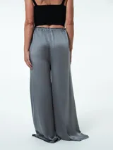 Pantalón negro de tela satinada, corte palazzo, cintura alta con elástico y lazo ajustable.