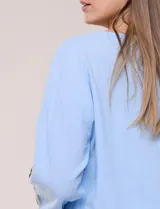 Blusa Erika de algodón con estampado de rayas en tonos azules, rosados y amarillos. Presenta cuello redondo con escote en V y botones frontales, mangas cortas decoradas con una fila de botones en los laterales y dobladillo asimétrico.