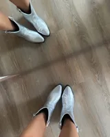 Bota estilo tejana de cuero vacuno en color plateado metalizado, con taco bajo cuadrado y costuras decorativas en la puntera.