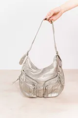 Bolso bandolera plateado de cuero sintético con múltiples bolsillos frontales con cierre.